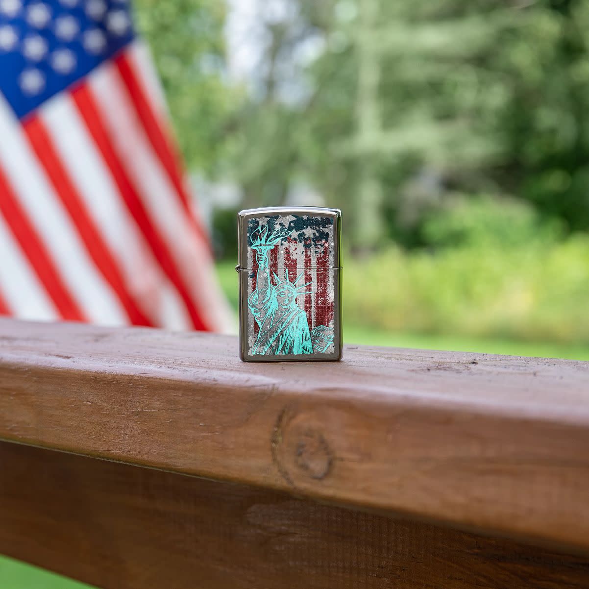 Lifestyle image of Statue Of Liberty Design Black Ice?« Windproof Lighter standing on a railing with an American Flag in the background.